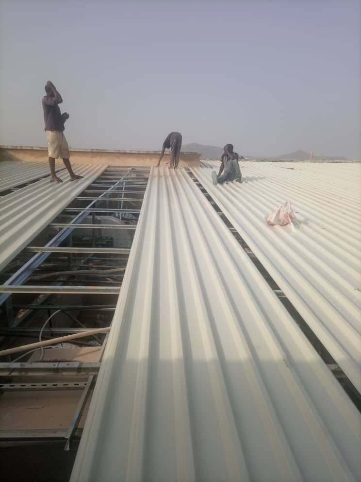 Team fitting white roofing sheets beside a skylight frame