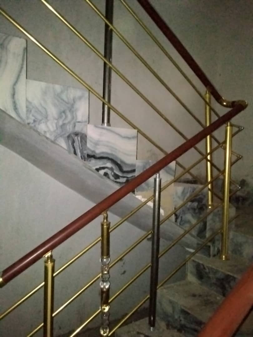 Gold-finish staircase railing with a wooden handrail over marble steps