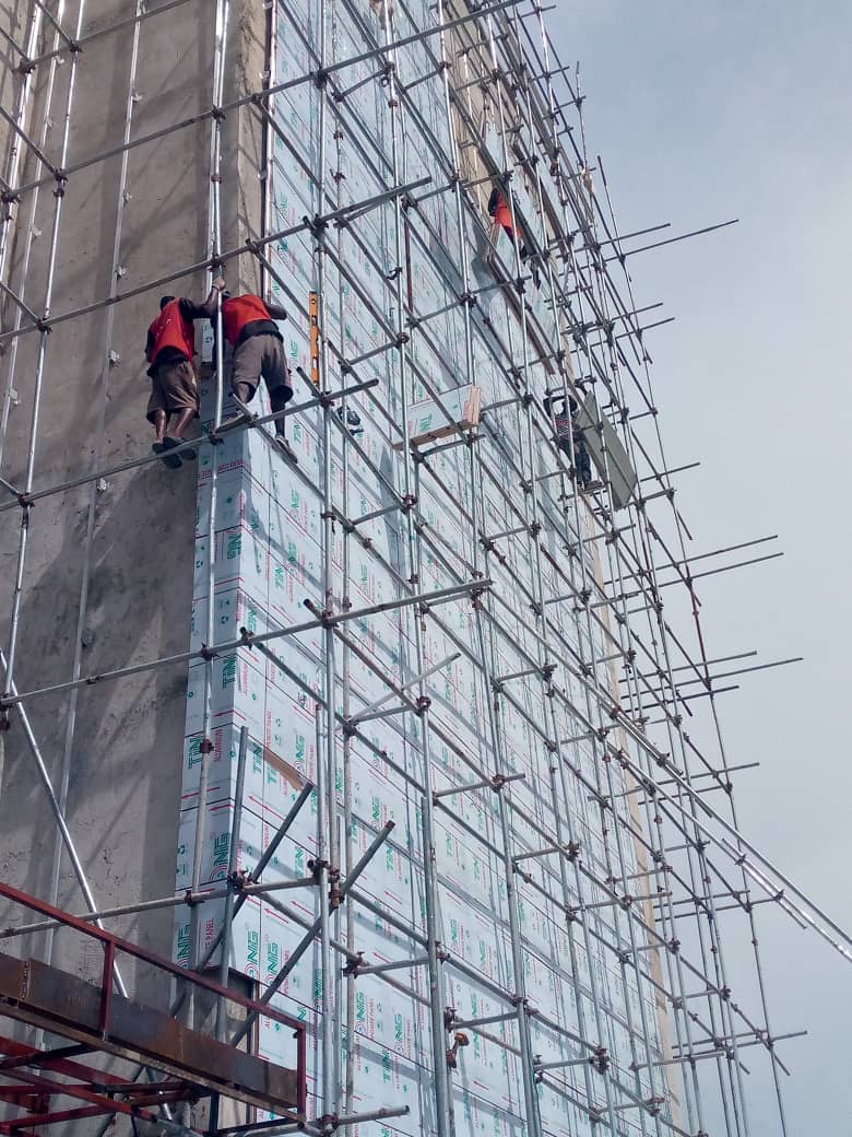 Workers fitting cladding panels from scaffolding